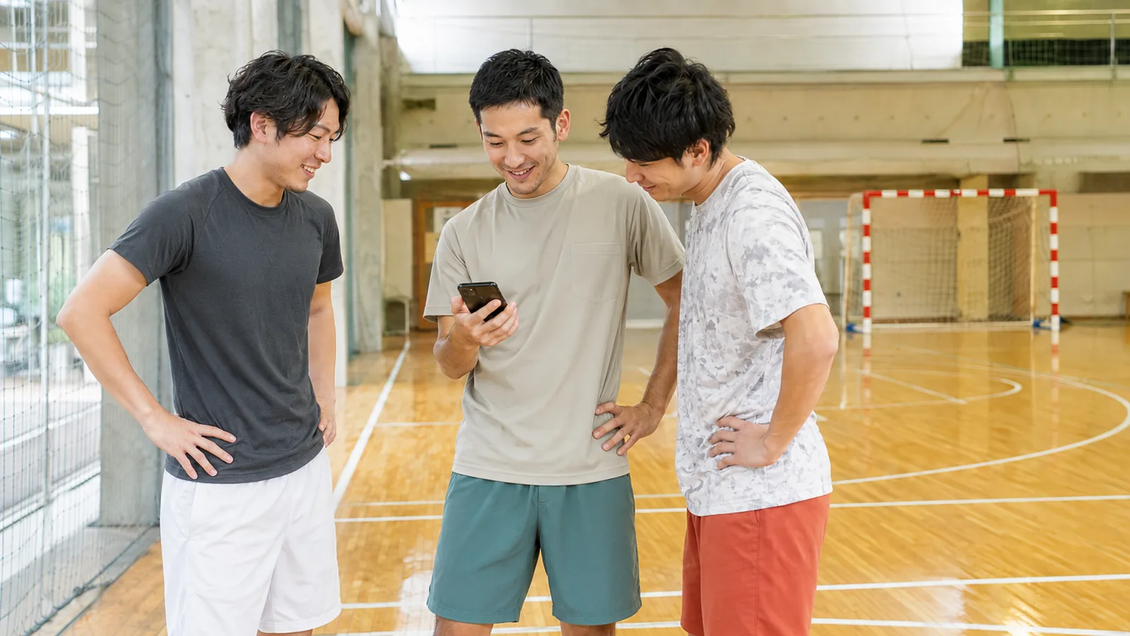 屋内フットサルコートの端で練習の合間に立ち話をしながらスマホを見る参加者たち